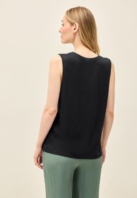 Top nero senza maniche in un tessuto morbido, con colletto rotondo e vestibilità rilassata, abbinato a pantaloni verde chiaro con texture.