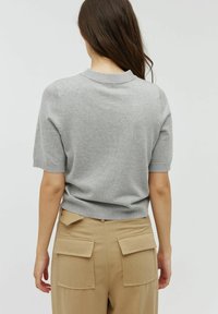 Krótki rękaw, jasnoszara dzianinowa sweter z okrągłym dekoltem i prążkowanym wykończeniem, zestawiony z beżowymi spodniami o wysokim stanie z tylnymi kieszeniami naszytymi.