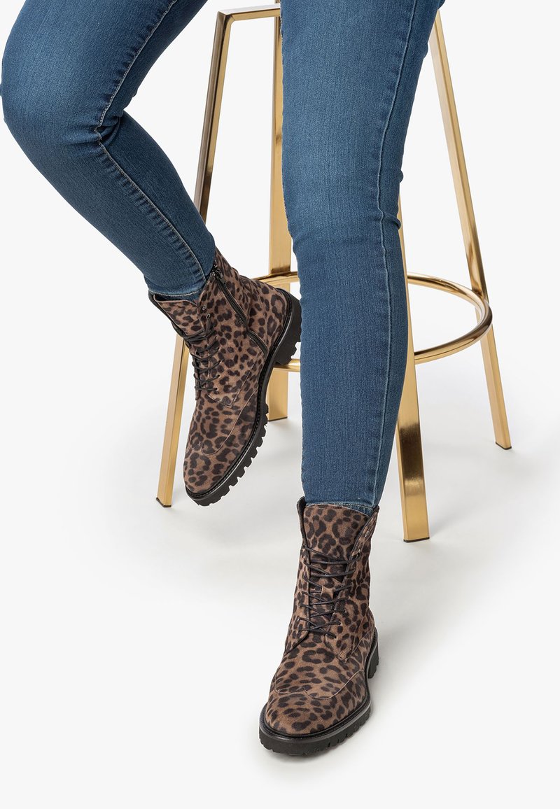 Botines de piel de animal con textura de ante, que presentan cordones negros, una suela robusta y un doblado en el puño, llevados con jeans skinny azules.