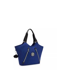 Sac fourre-tout bleu avec une large ouverture, poignées noires, deux zips à l'avant et un patch logo rond. Comprend un accessoire en pompon en fourrure.