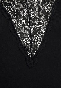 Top preto com um design de decote em V de renda, apresentando padrões florais intrincados e bordas recortadas, contrastando com uma textura de tecido sólida.