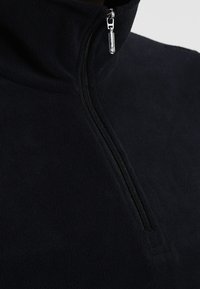 Svart fleece tröja med kvartdragkedja som har en hög krage och silverfärgad dragkedja, med en mjuk textur och slät yta.