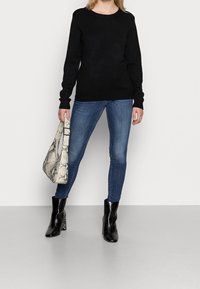 Svart stickad tröja, blå tajta jeans, svarta klackade ankelstövlar och en grå handväska med ormskinnsmönster. Enkel design, slät textur.