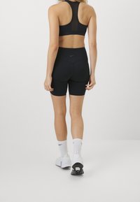 Brassière de sport noire avec panneau en mesh et shorts noirs assortis. Chaussettes blanches et baskets. Design simple et ajusté sans motifs visibles.