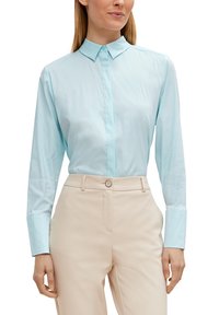 Himmelblaues Langarmbluse mit einem Button-Down-Kragen, aus glattem Stoff gefertigt, kombiniert mit beigen maßgeschneiderten Hosen.