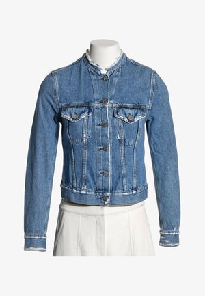 Veste en denim bleu à manches longues, fermeture boutonnée sur le devant, deux poches poitrine à boutons et un col effiloché sur un mannequin.