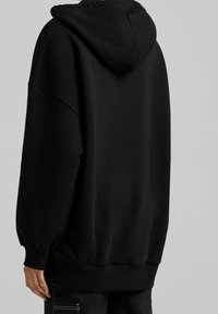 Felpa nera oversize, in cotone, con una consistenza morbida, polsini e orlo a costine, dotata di cappuccio e spalle scese, design minimalista.