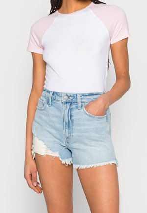 Witte top met korte mouwen en lichtroze raglanmouwen, gecombineerd met verknipte denim short in lichtblauw, voorzien van een rafelige zoom en zijzakken.