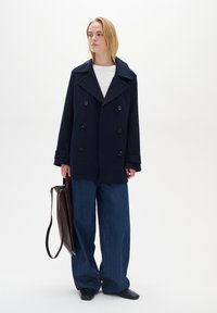 Palton bleumarin cu două rânduri de nasturi, cu rever mari, asortat cu o cămașă albă și pantaloni din denim albastru cu croială largă. Geantă din piele maro cu o bandă lungă.