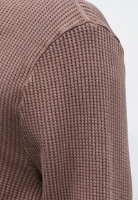 Brunt tekstureret strikket stof med et gittermønster. Nærbilledet viser det vævede detalje og den let hævede overflade af materialet.