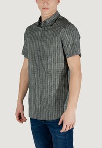Camicia a maniche corte, con bottoni, di colore nero con un motivo geometrico bianco. Tessuto morbido, colletto e vestibilità rilassata. Adatta per un abbigliamento casual.