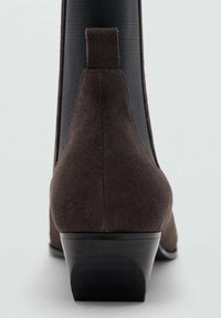 Stivaletto in suede marrone con lato elastico nero, tacco basso a blocco e design minimalista. La texture liscia e le linee pulite ne esaltano l'aspetto.