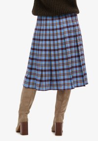 Jupe plissée longueur genou en bleu ciel avec un motif à carreaux violet foncé et jaune. Associée à des bottes hautes en daim beige.