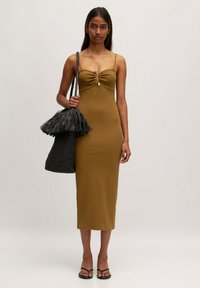 Olivegrünes, eng anliegendes Kleid mit einer geknoteten Frontpartie, dünnen Trägern und midi Länge. Kombiniert mit einer strukturierten schwarzen, gewebten Tasche und Sandalen.