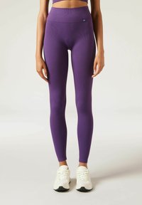 Paarse geribde leggings met een hoge taille, een gladde textuur en logodetails. Gecombineerd met witte sportschoenen met zwarte accenten.