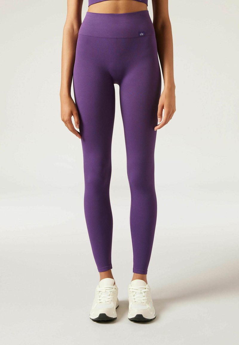 Paarse geribde leggings met een hoge taille, een gladde textuur en logodetails. Gecombineerd met witte sportschoenen met zwarte accenten.