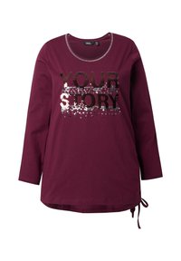 Bordeauxfarbenes Langarm-T-Shirt mit Rundhalsausschnitt, das ein Pailletten-Design zeigt, das "DEINE GESCHICHTE" auf der Vorderseite schreibt. Mit seitlichen Bindebändern.