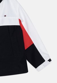 Kurtka w kolorowe bloki z czarnymi, białymi i czerwonymi elementami. Wykonana z gładkiego, wytrzymałego materiału z teksturowanym kołnierzem i mankietami.