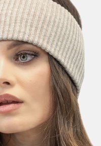 Beige ribbet strik hovedbånd med en blød tekstur, der har et bredt design, der dækker ørerne og tilføjer varme og komfort.