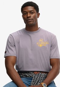 Camiseta gris de manga corta con un gráfico amarillo de "Super Dry". Tejido de algodón con un escote redondo y una textura sutil.