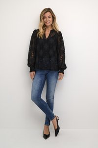 Črna čipkastaj bluzica z V-izrezom in napihnjenimi rokavi, v kombinaciji s svetlo modrimi ozkimi kavbojkami in črnimi čevlji s koničastim nosom.