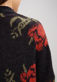 Suéter de punto con un fondo oscuro y patrones florales en rojo y verde, textura suave y diseño de cuello redondeado.