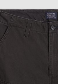 Gros plan sur la ceinture d'un pantalon noir Levi's montrant la boucle de ceinture, le bouton avec le logo Levi's, le bord de la poche avant et l'étiquette cousue avec le nom de la marque.