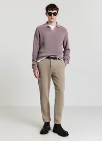 Maglione lavorato a maglia a costine viola chiaro, maglietta bianca a girocollo sotto, pantaloni a costine beige e stivaletti neri alla caviglia. Occhiali da sole neri.