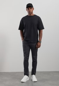 Musta puuvillainen t-paita, rento istuvuus, yhdistetty tummiin housuihin ja valkoisiin lenkkareihin. Asusteina musta lakki ja hopeinen rannekello.