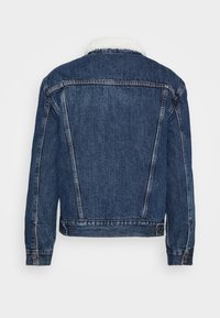 Veste en jean bleu foncé avec col sherpa blanc, coutures visibles, poignets boutonnés et pattes latérales réglables, vue de dos.