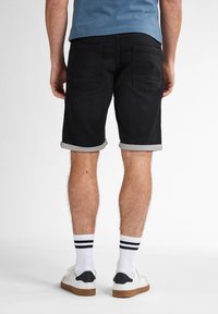 Schwarze Denim-Shorts mit umgeschlagenen Säumen, zwei Gesäßtaschen und glatter Textur, kombiniert mit weißen Socken mit schwarzen Streifen und lässigen Turnschuhen.