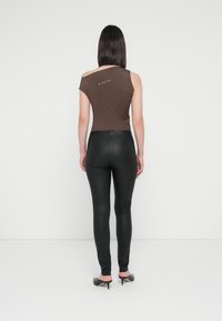 Top marron ajusté avec un design décolleté et une marque blanche, associé à des leggings noirs brillants et des chaussures à talons noires.