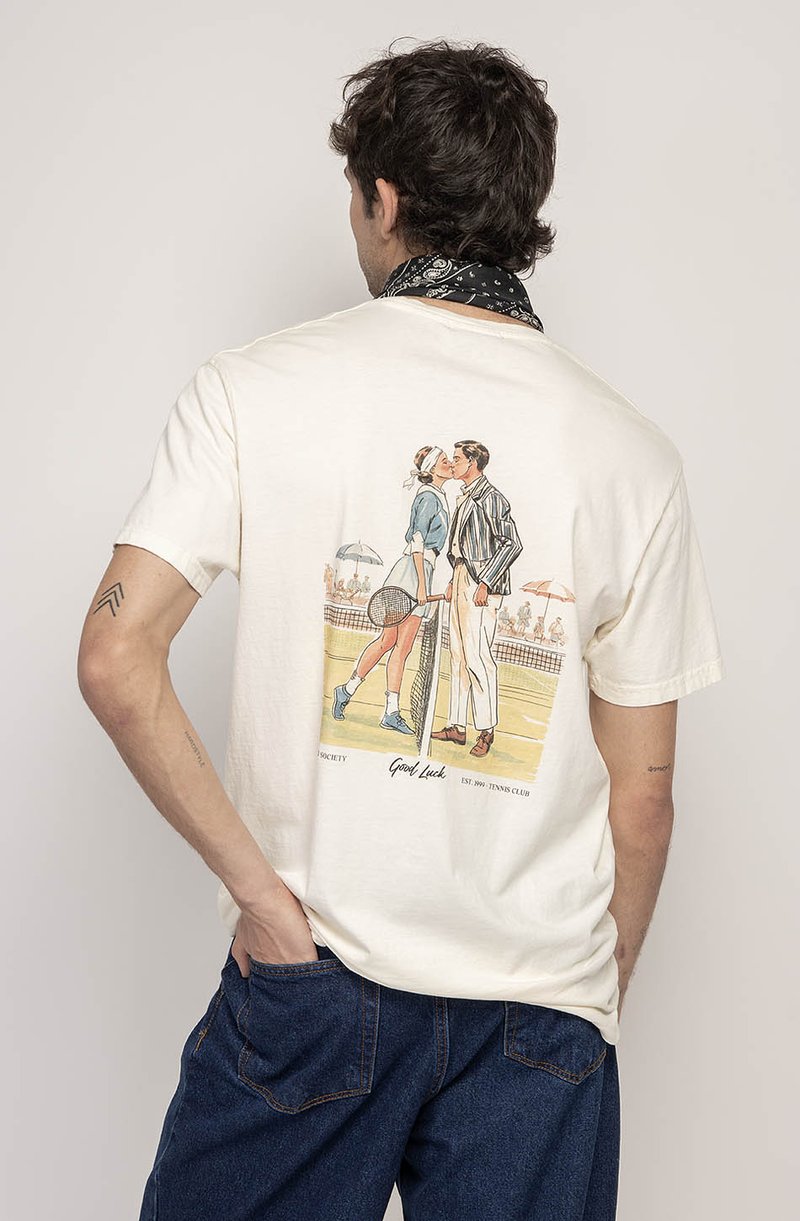 Kreminė medvilninė marškinė su retro teniso tema grafika ant nugaros, vaizduojanti porą, apsikabinusią, apsuptą korto scenos.