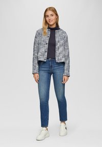 Gewebte blaue und weiße Tweedjacke mit taillierter Form, kombiniert mit dunklen Jeans und weißen Sneakers. Verfügt über einen runden Halsausschnitt und eine Knopfleiste vorne.
