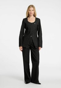 Svart denimjacka med rundad halsringning, långa ärmar och knappstängning, i kombination med vida svarta denimbyxor.