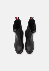 Botas de tobillo de cuero negro con un acabado suave, que cuentan con paneles laterales de tela y tiradores rojos, blancos y azules en la parte posterior.