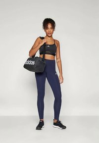 Reggiseno sportivo nero, leggings blu navy, sneakers nere. Borsa a tracolla nera con logo Adidas bianco. Tessuto morbido, design aderente.