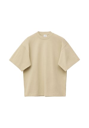 T-shirt beige oversize à manches courtes et col rond, étalé à plat, avec des coutures visibles sur les manches et l'ourlet, sur fond blanc.