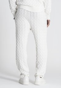 Witte gebreide sweatpants hebben een textuur met kabelpatroon, ribgebreide manchetten en een elastische tailleband. Gestyled met witte sneakers.