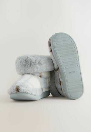 Zapatillas de felpa de color azul claro con un puño de piel sintética, adornadas con un patrón blanco y marrón, que cuentan con una suela de goma texturizada y un material suave y grueso.