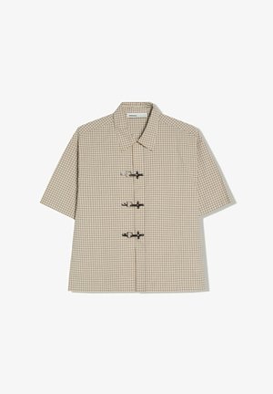 Chemise à manches courtes à carreaux beige et blanc avec col et trois fermetures métalliques à bascule sur le devant.