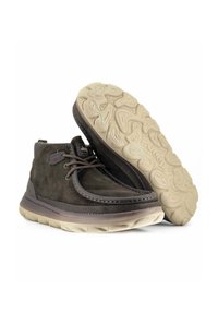 Stivali alla caviglia in suede marrone con suola in gomma beige flessibile, caratterizzati da punta arrotondata, dettagli cuciti e design con lacci. Logo sul lato.