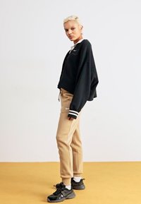 Melns īsais treniņjakas krekls ar baltām līnijām pie aprocēm, apvienots ar bēšiem šauriem treniņbiksēm. Melnas sporta apavi ar pelēkiem akcentiem.