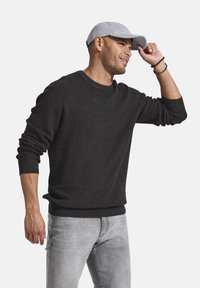 Dunkelgrauer, gerippter Pullover mit langen Ärmeln und rundem Ausschnitt, kombiniert mit hellgrauen Jeans. Eine hellgraue Kappe wird rückwärts getragen.