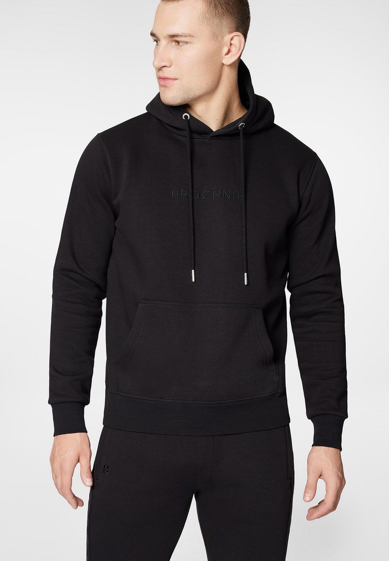 Czarna hoodie z kapturkiem wykonana z gładkiego materiału. Posiada kieszeń na przodzie, regulowane sznurki oraz wytłoczone logo "PROCHNIK" na klatce piersiowej.