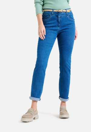 Blaue Jeans im geraden Schnitt mit hochgekrempelten Säumen und Fronttaschen, kombiniert mit beigen Slippers und einem hellgrünen Pullover.