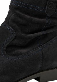 Černé semišové kotníkové boty s nashromážděnou texturou, modrými švy, zaobleným střihem u kotníku a masivním podpatkem.