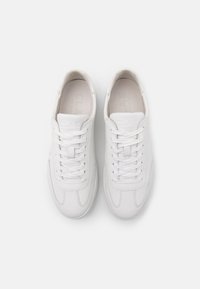 Paire de baskets en cuir blanc avec lacets, placées côte à côte sur un fond clair uni, vue de dessus.