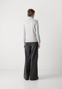 Jasnoszary sweter z wysokim kołnierzem, prążkowanymi mankietami i dół, zestawiony z luźnymi, ciemnoszarymi spodniami. Prosty i minimalistyczny design.