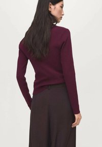 Pull bordeaux au design ajusté, avec des poignets côtelés et un ourlet arrondi. Associé à un pantalon évasé marron foncé, mettant en valeur une silhouette épurée.